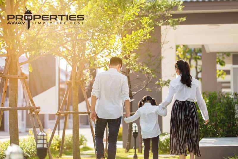 A family walking hand in hand outside a modern house with a tropical garden